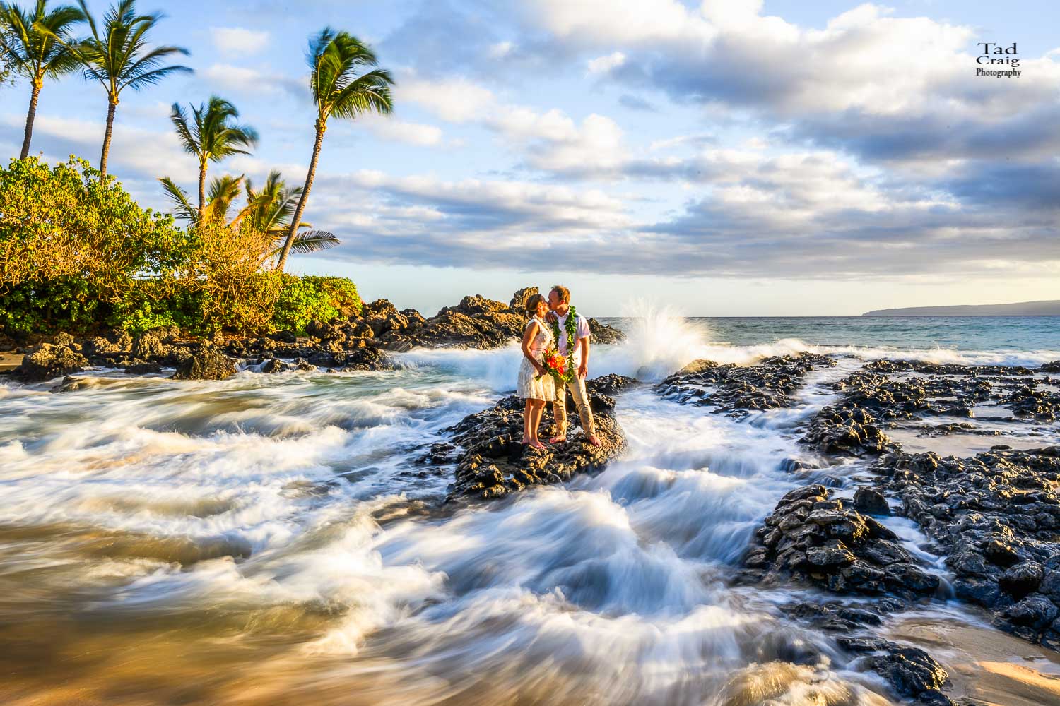 Just married couple kissing as water surrounds them on a beach in Maui Hawaii