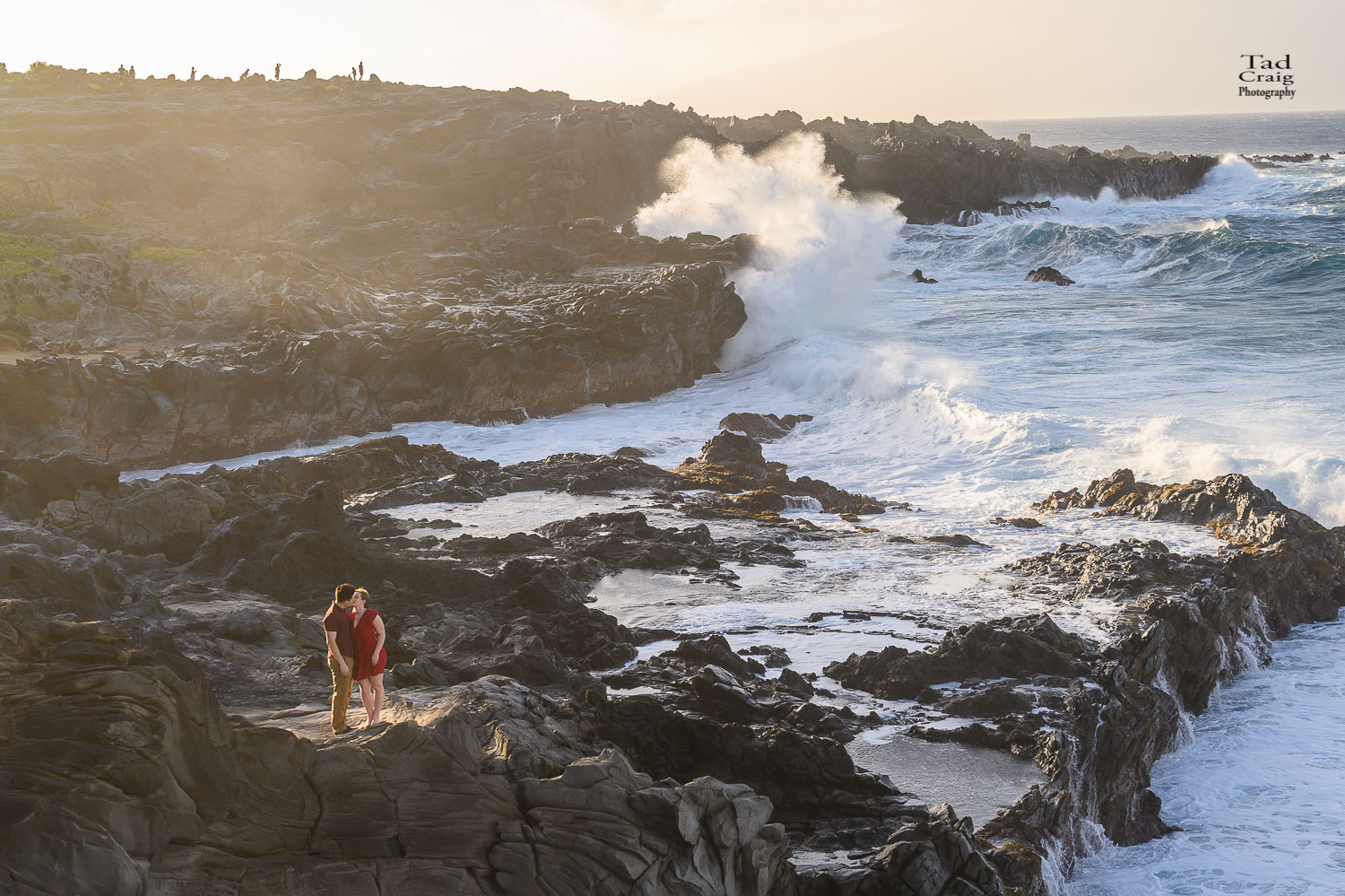 Just Engaged couple kissing on rocks with huge Maui waves breaking behind them