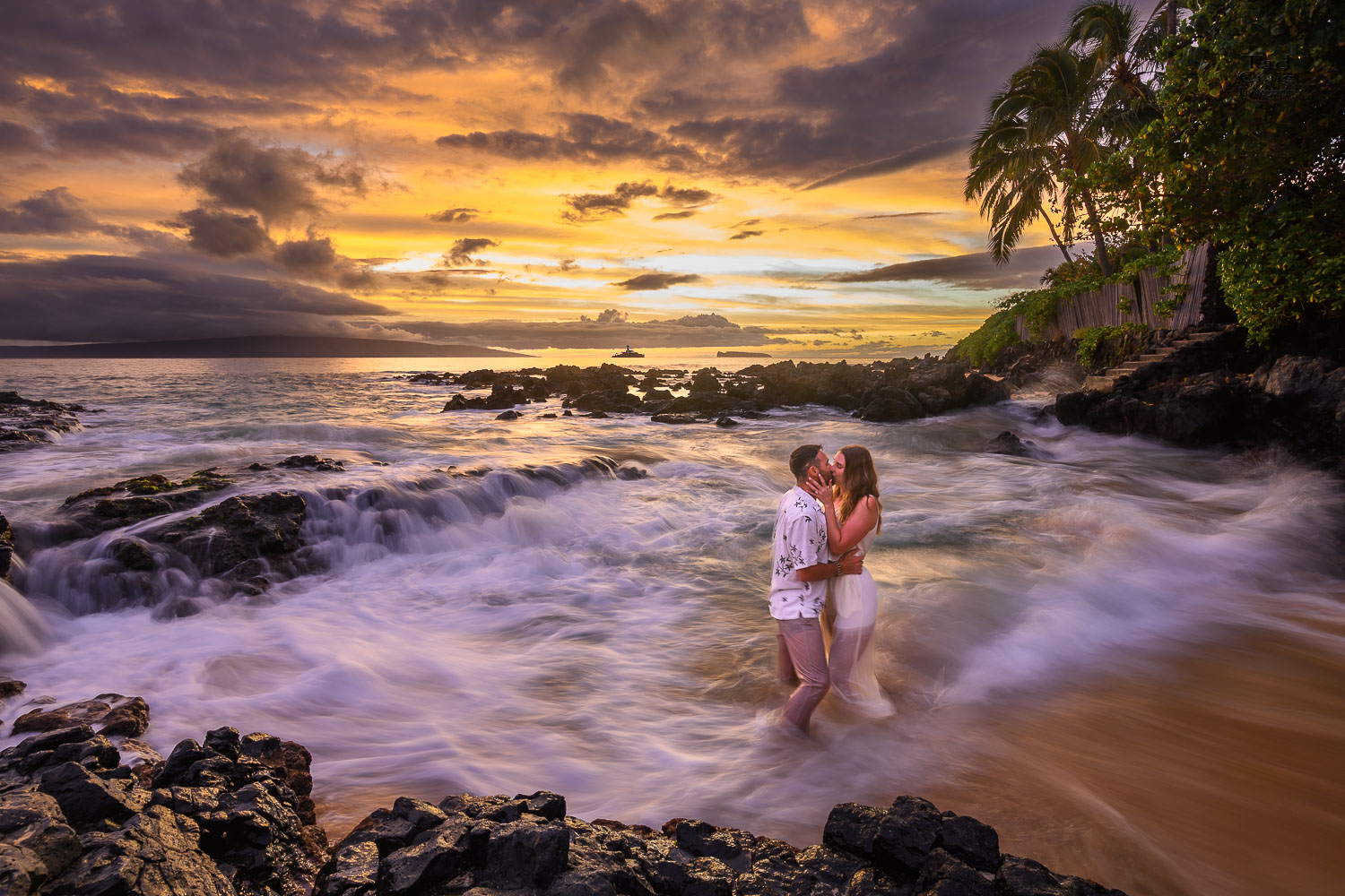 Just engaged couple kissing in the ocean as a beautiful sunset behind them explodes in color